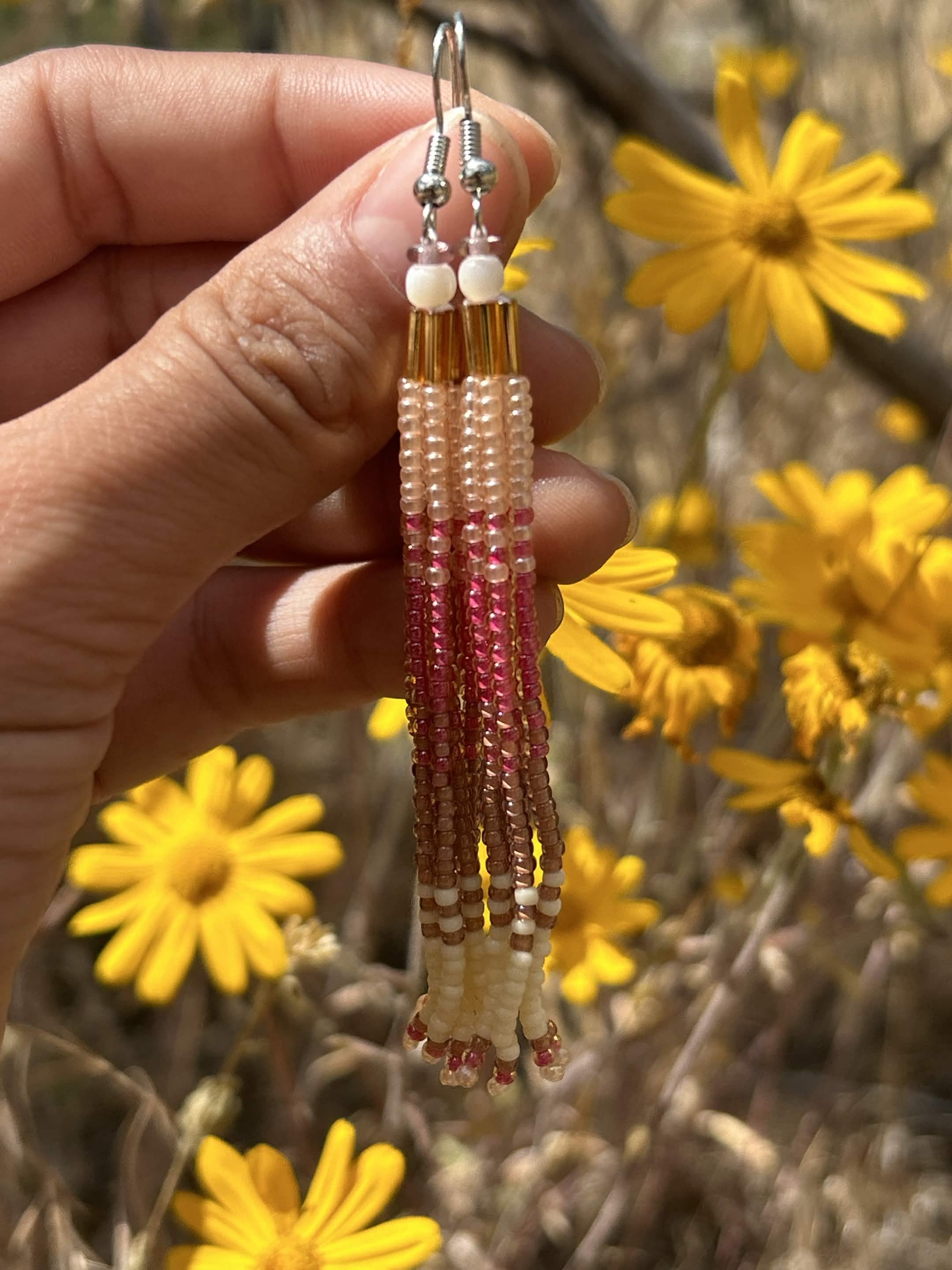 Golden bloom tassel earrings held against yellow wildflowers in a sunny field